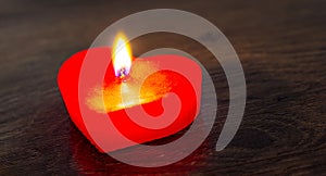 Lighted red candle in the form of a heart on a dark wooden background. Free space for text_