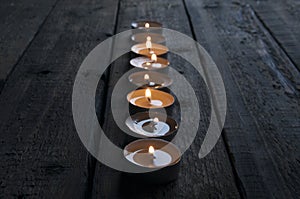 Lighted small candles laid out in a row on a wooden table. Texture. Symbol. Holidays love day