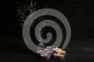 Lighted small candles laid out in a row on a wooden table. Texture. Symbol. Vase with green branches. Still life