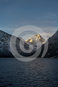 Lighted snowy mountain peak thaneller at lake plansee