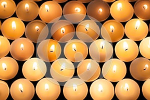 Lighted tealight candlelight background image. Lit flaming candles in rows from above.