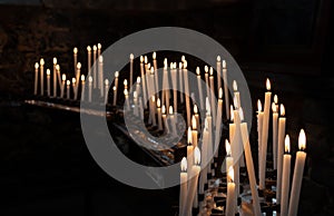 Lighted thin church candles stand in large numbers in a dark room