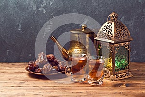 Lightened lantern, tea cups and dates on wooden table over blackboard background. Ramadan kareem holiday celebration