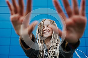 Lighthearted teenage girl blocking camera with hands in front of a blue panel