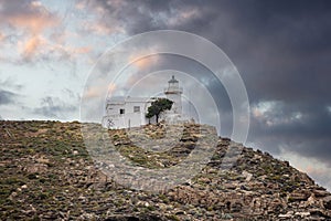 Kea island, Greece. Lighthhouse Tamelos on a rocky cliff, cloudy sky background