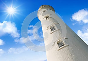 Low angle view of a lighthouse against blue sky with clouds and sun