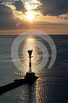 Lighthouse and a boat over the calm sea on sunset