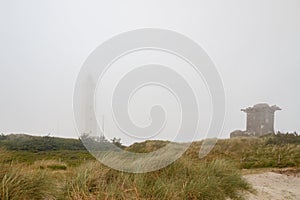 Lighthouse and bunker in the sand dunes on the beach of Blavand in fog, Jutland Denmark Europe