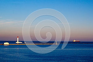 Lighthouse and Cargo ship leaving a harbor in the evening