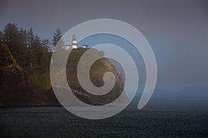 Lighthouse on cliff above foggy calm ocean