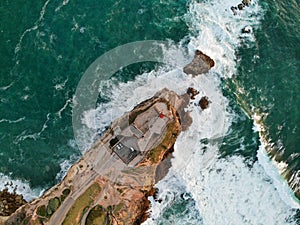 Lighthouse on a cliff rock with giant waves. ocean or sea. Aerial drone view.