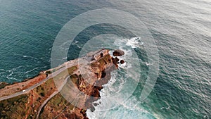 Lighthouse on a cliff rock with giant waves. ocean or sea. Aerial drone view.