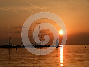 Lighthouse at the end of the pier of stones, sunset over the Adriatic Sea, Croatia, Europe.Orange, calm sea, silhouette, reflectio