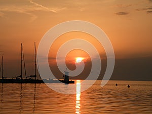 Lighthouse at the end of the pier of stones, sunset over the Adriatic Sea, Croatia, Europe.Orange, calm sea, silhouette, reflectio