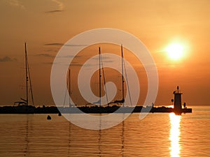 Lighthouse at the end of the pier of stones, sunset over the Adriatic Sea, Croatia, Europe.Orange, calm sea, silhouette, reflectio