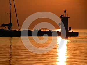 Lighthouse at the end of the pier of stones, sunset over the Adriatic Sea, Croatia, Europe.Orange, calm sea, silhouette, reflectio