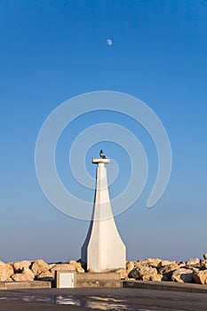 Lighthouse At The Entrance To The Marina On A Background Of Blue Sky With The Moon