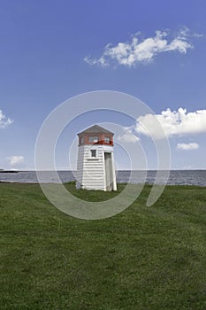 Lighthouse on grass with blue sky and ocean background