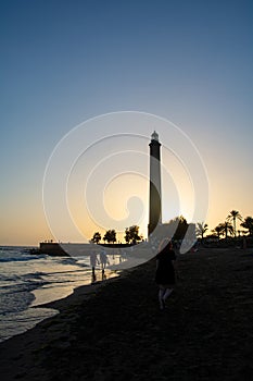 Lighthouse in Maspalomas, Gran Canaria, Spain at sunset with a girl on beach