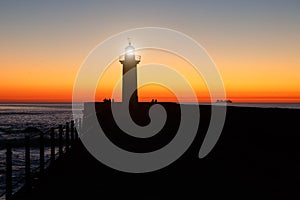 Lighthouse on the ocean, silhouette at sunset.