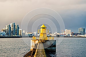 Lighthouse in reykjavik, iceland. Lighthouse tower and stone pier in sea. Seascape and skyline on grey sky. Architecture