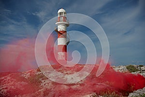 A lighthouse on a rocky coast in Cancun with a red smoke screen. Mexico.