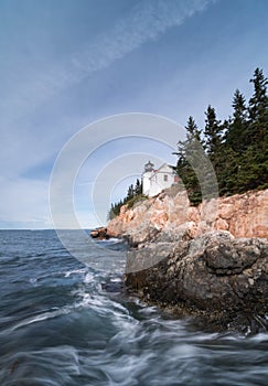 Lighthouse on a rocky coast with crashing waves in the foreground