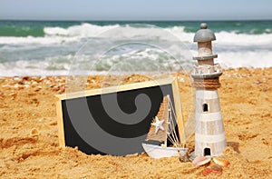 Lighthouse, sailboat and chalkboard, on sea sand and ocean horizon