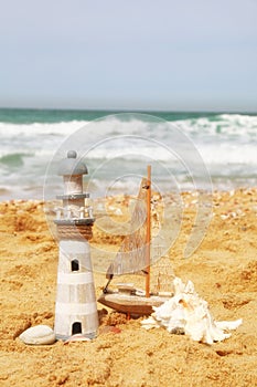 Lighthouse, sailboat on sea sand and ocean horizon.