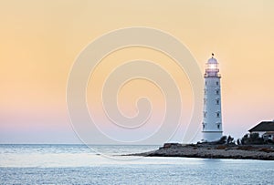 Lighthouse searchlight beam near ocean at sunset