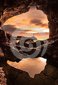 Lighthouse seen from inside a cave with a puddle reflecting the sky