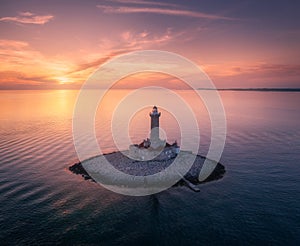 Lighthouse on smal island in the sea at colorful sunset in summer