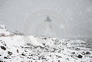 Lighthouse in Snowstorm by Rocky Coast in New England