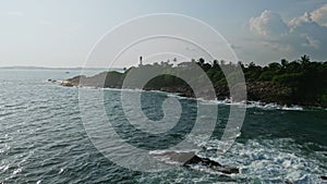 Lighthouse stands on a hill, overlooking waves hitting rocky shore. Scene captures maritime guidance, travel destination