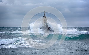 Lighthouse and storm in the sea and large waves that break into the sea light at the port of Ahtopol, Black Sea, Bulgaria