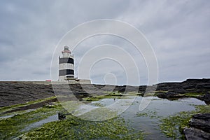 Lighthouse surrounded by rocks with moss and reflections in the water. Wexford, Ireland