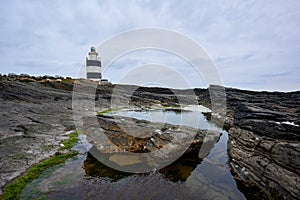 Lighthouse surrounded by rocks with moss and reflections in the water. Wexford, Ireland