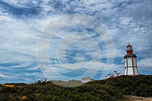Lighthouse on top of cliff and surrounded by vegetation at Cape Espichel