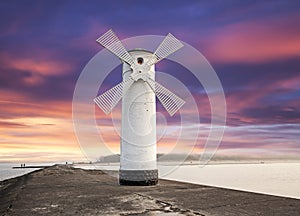 Lighthouse windmill with dramatic sunset sky.