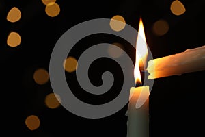 Lighting candle from another one against blurred lights in darkness, closeup. Space for text photo