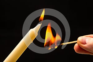 Lighting a candle with a wooden match on a dark background. Burning candle fire