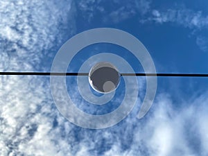 Lighting lamp hanging on electric cable on blue sky background.