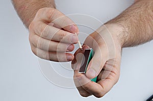 Lighting a match. Close-up of hands, matchbox and match on light-gray bsckground