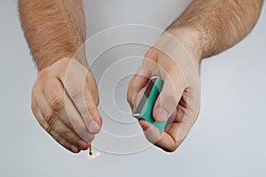 Lighting a match. Close-up of hands, matchbox and match on light-gray bsckground