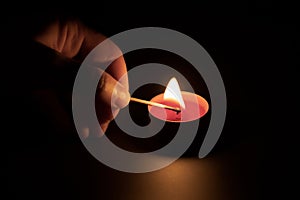 Lighting a red candle with a match in the dark. Memory concept. Black background