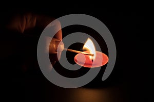Lighting a red candle with a match in the dark. Memory concept. Black background.