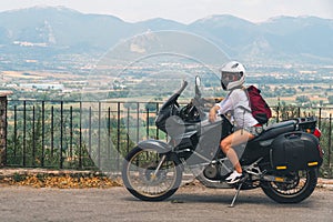 A lightly dressed girl is sitting on a motorcycle. No protection. Helmet. Sunny day in Narni, Italy. Green mountains in the