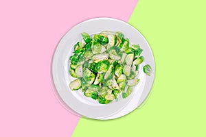 Lightly fried brussels sprouts on a white plate on the neon green and pink color drop
