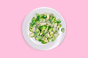 Lightly fried brussels sprouts on a white plate on the solid pink color drop