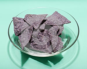 Lightly Salted Organic Blue Corn Tortilla Chips in clear glass bowl isolated on green